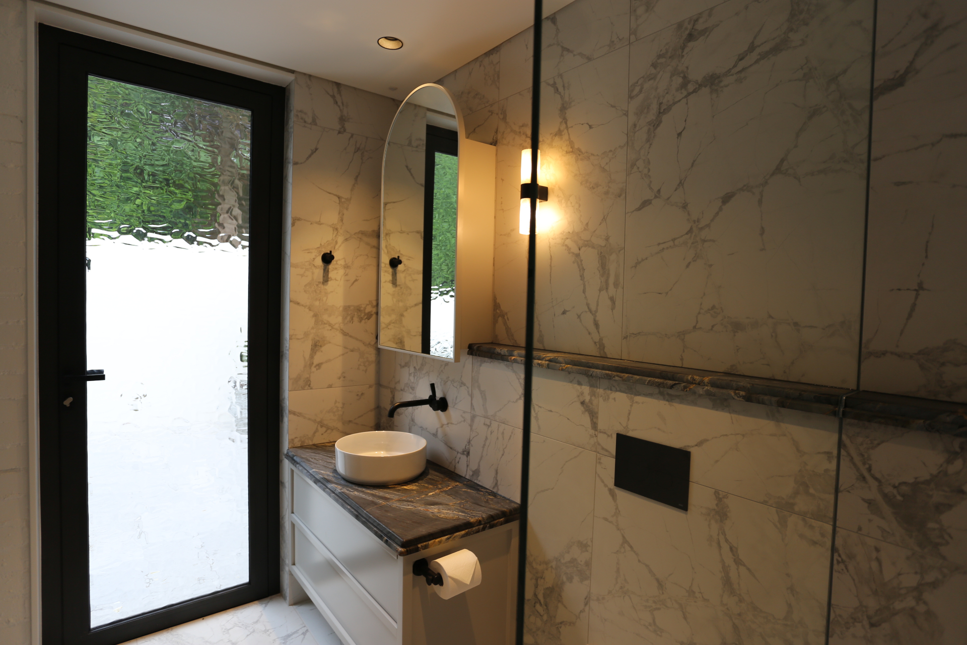 Ensuite vanity with marble-look wall lining, dark stone top and feature lighting by Mr Woodworx