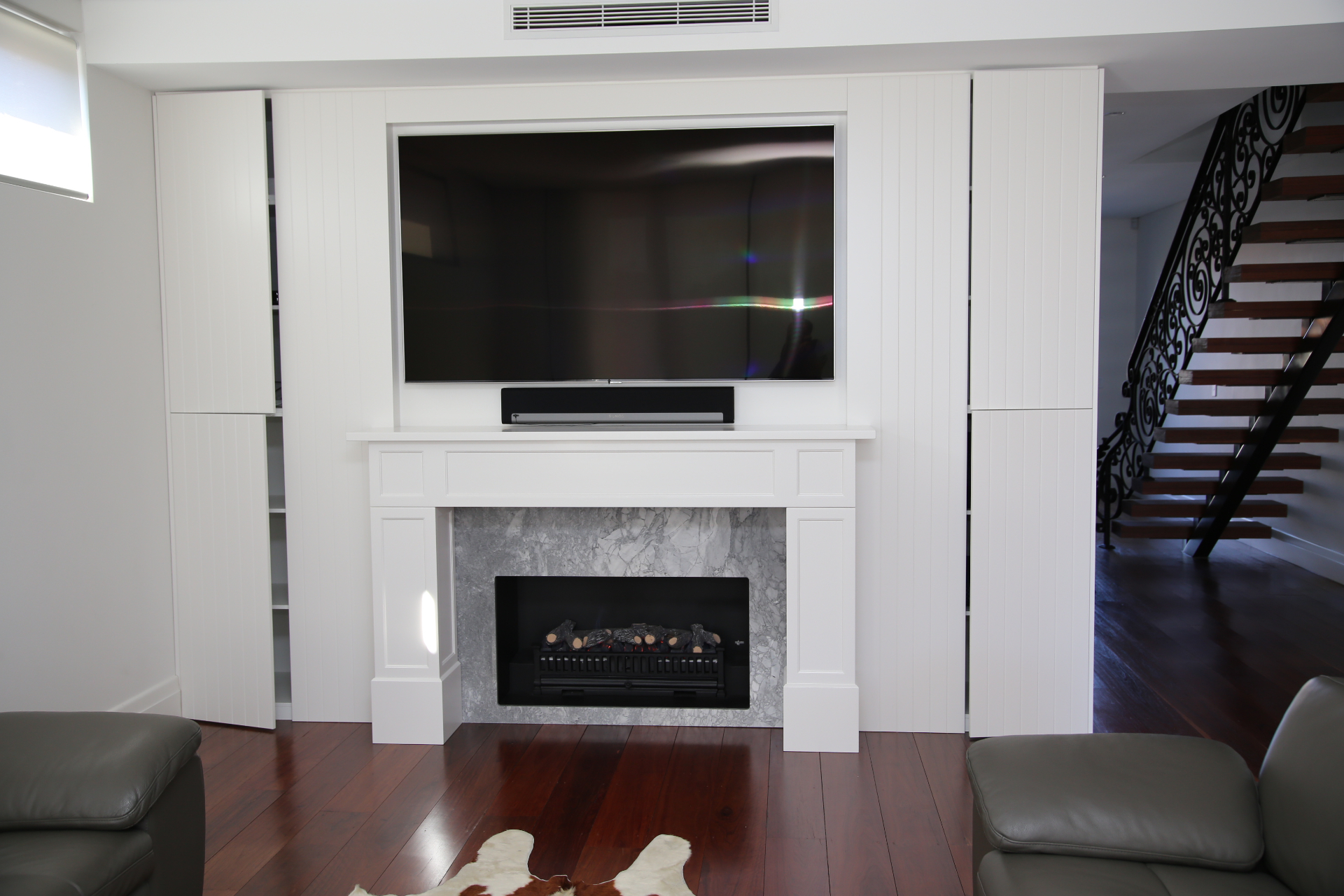 White panelled media wall with marble fireplace surround, mounted TV and concealed cabinetry by Mr Woodworx