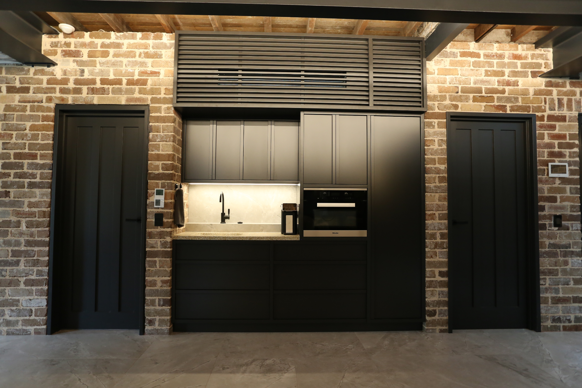 Matte black cabinetry kitchenette set against recycled brickwork by Mr Woodworx