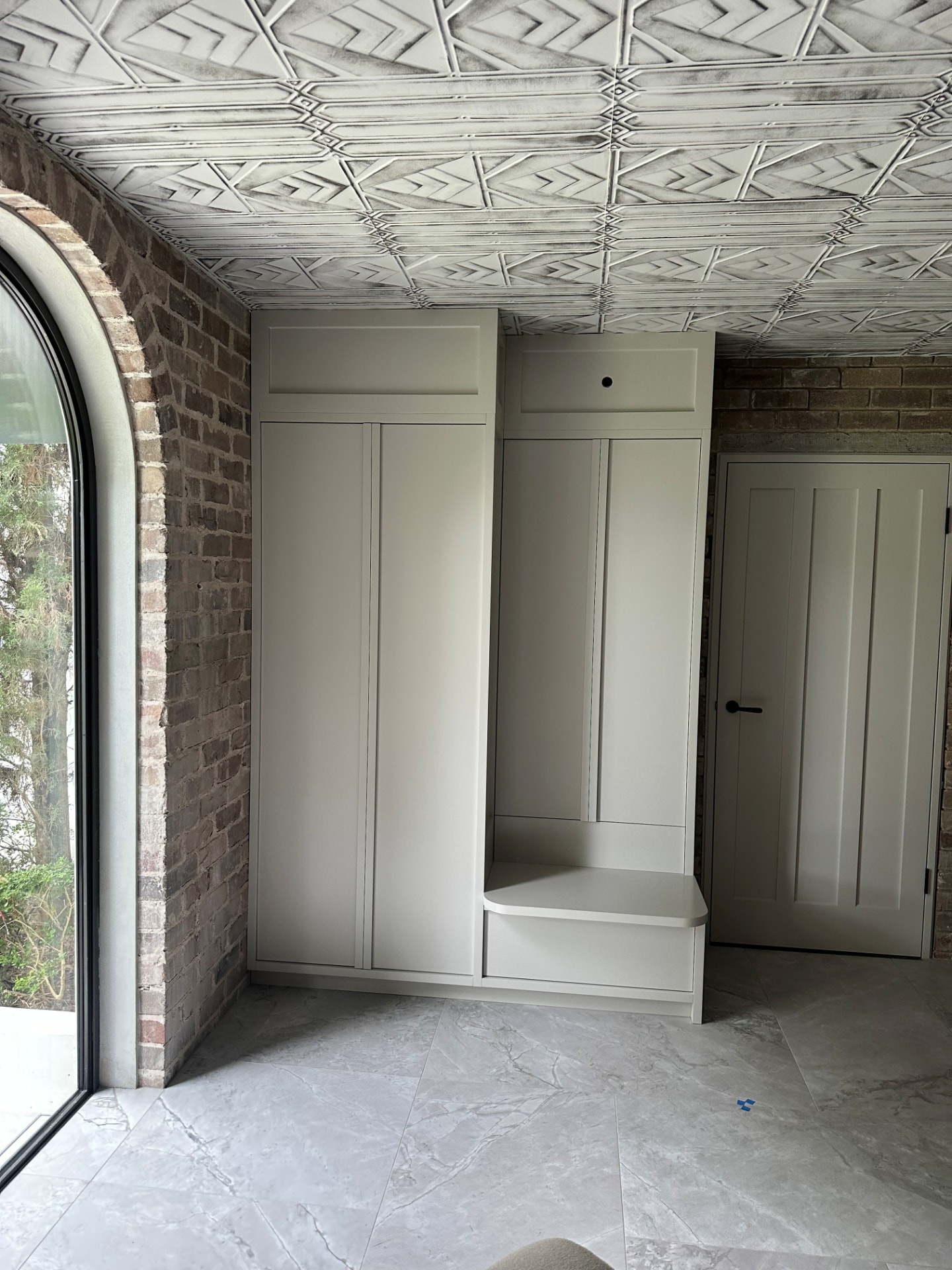 Custom painted mudroom joinery with bench seat and tall storage against recycled brick and a pressed-tin ceiling in Cremorne by Mr Woodworx