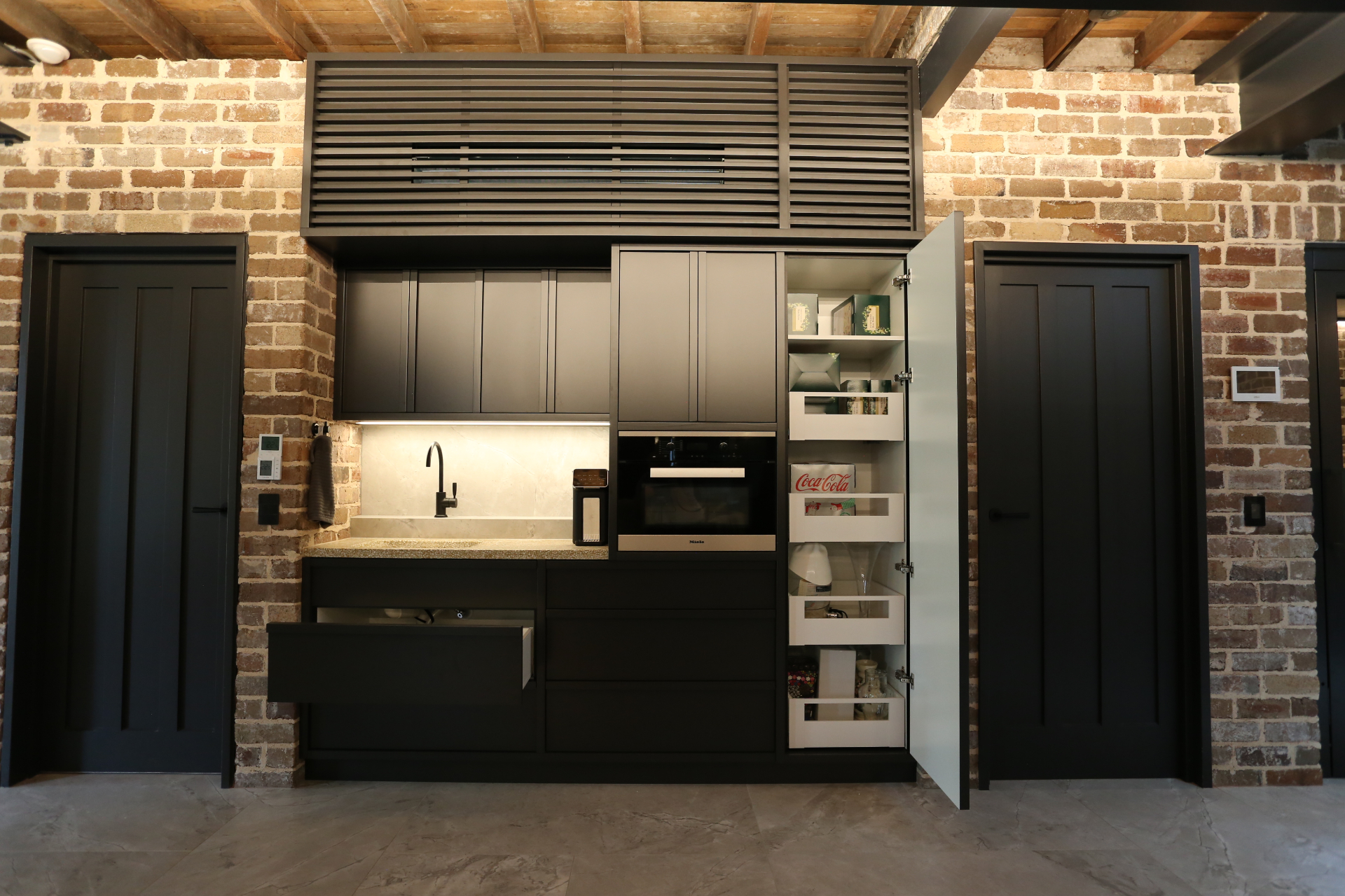 Matte black kitchen with integrated appliances and pull-out pantry storage by Mr Woodworx
