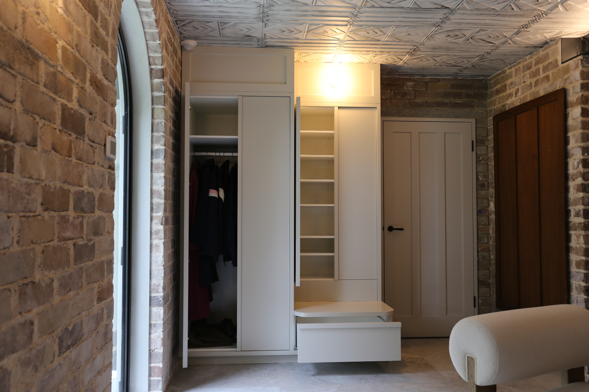 Custom white mudroom joinery with hanging space, shelving and bench seat against exposed brick by Mr Woodworx