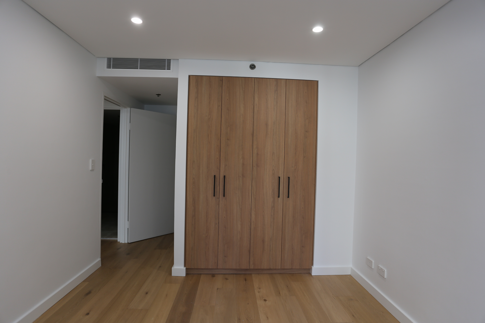 Floor-to-ceiling built-in timber wardrobe with matte black handles in a bedroom by Mr Woodworx