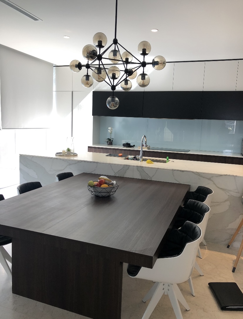 Modern kitchen with marble waterfall island, blue glass splashback and integrated dining table by Mr Woodworx