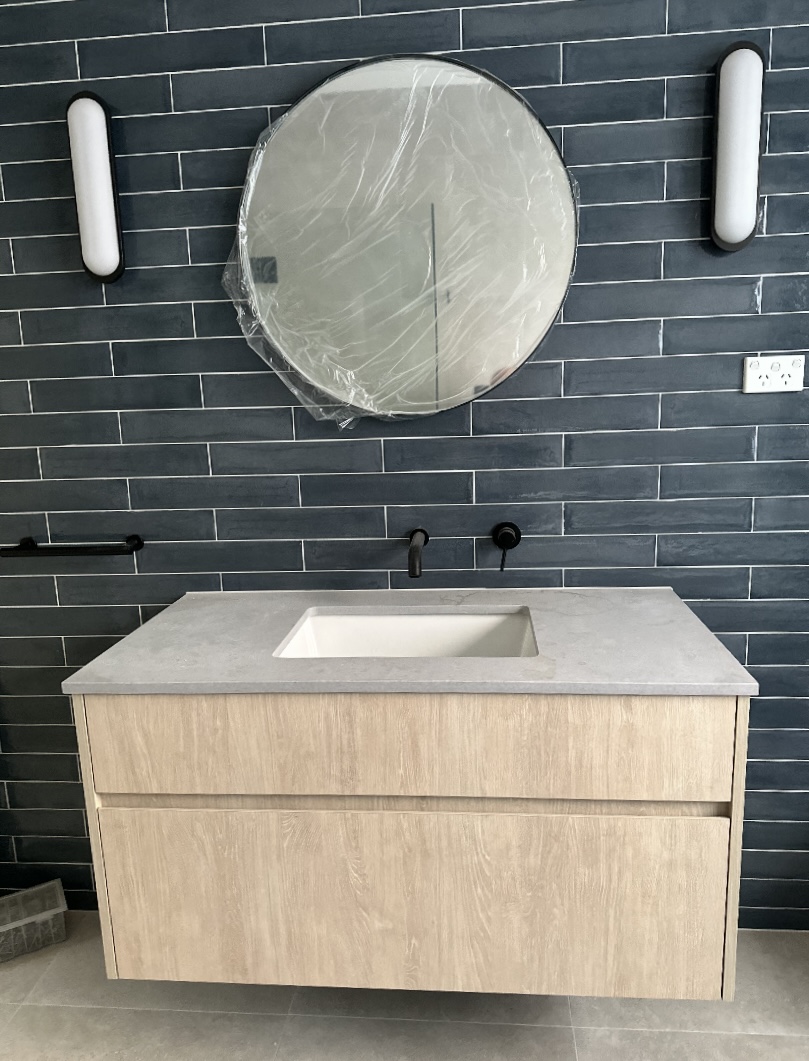 Oak floating vanity with stone top, undermount basin and charcoal brick-tiled wall by Mr Woodworx